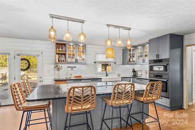 kitchen featuring hanging light fixtures, light hardwood / wood-style flooring, gray cabinets, double oven, and a center island