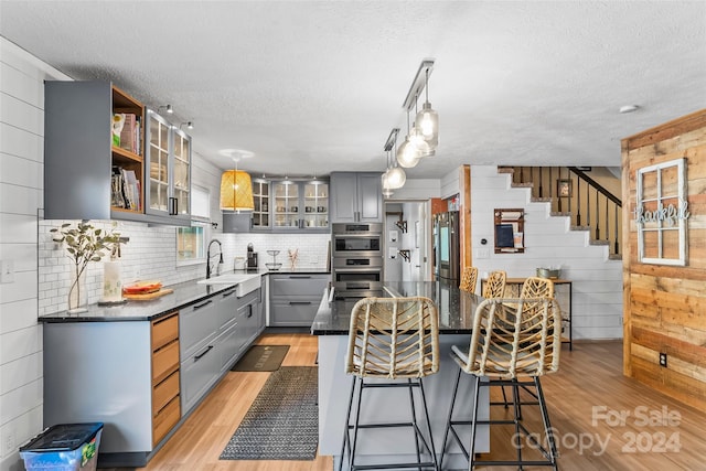 kitchen featuring gray cabinets, light hardwood / wood-style flooring, hanging light fixtures, and wood walls