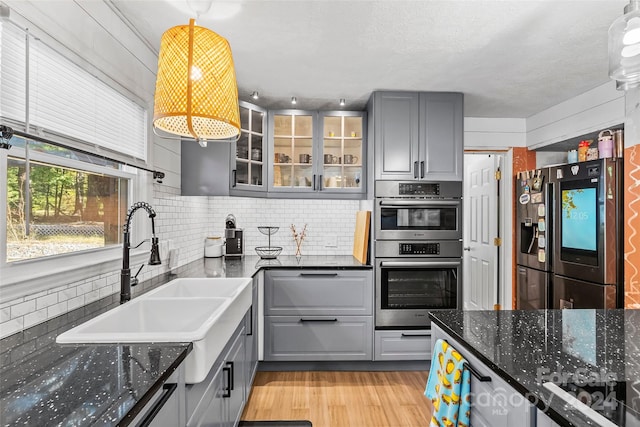 kitchen featuring decorative backsplash, stainless steel appliances, dark stone counters, sink, and pendant lighting