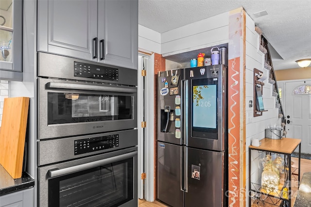 kitchen featuring a textured ceiling, appliances with stainless steel finishes, gray cabinetry, and light wood-type flooring