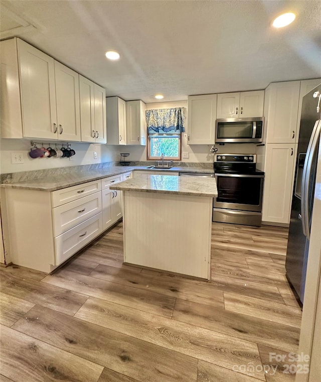 kitchen with light wood-type flooring, appliances with stainless steel finishes, a kitchen island, light stone countertops, and white cabinets