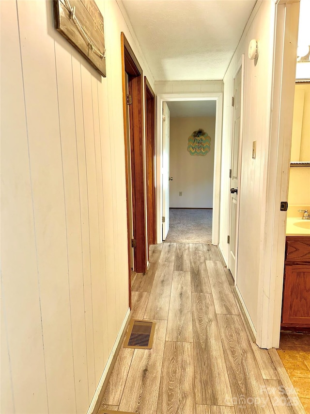 hall featuring sink, wooden walls, and light wood-type flooring