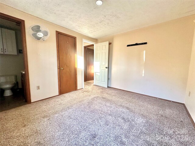 unfurnished bedroom featuring ensuite bathroom, carpet, and a textured ceiling