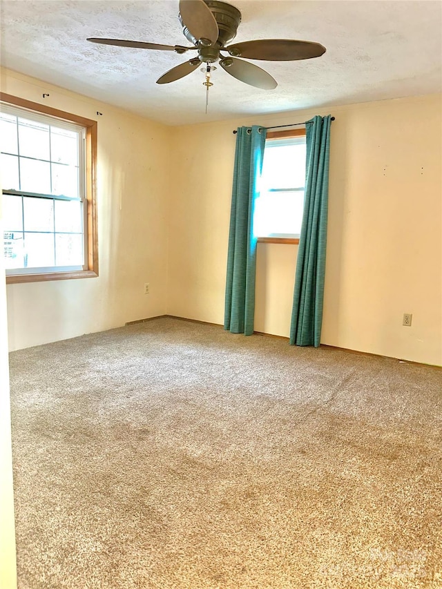 carpeted spare room featuring ceiling fan, a textured ceiling, and a healthy amount of sunlight