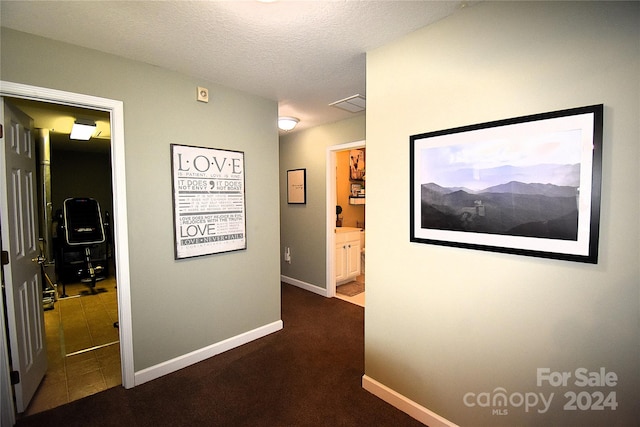 hallway featuring a textured ceiling and dark colored carpet