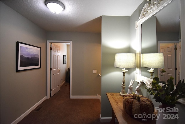 hallway with a textured ceiling and dark carpet