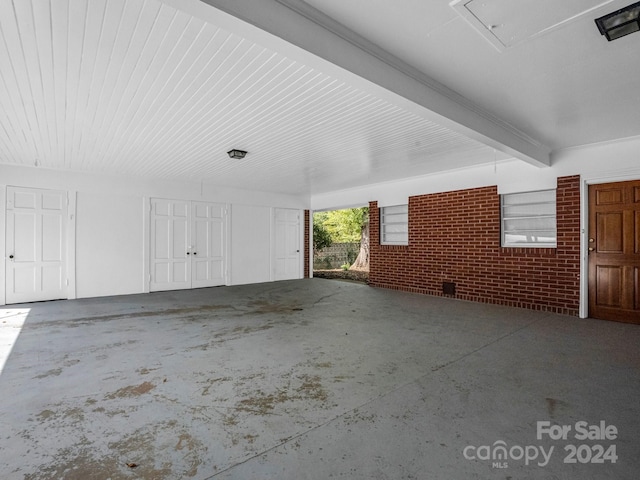 interior space featuring beamed ceiling, unfinished concrete flooring, attic access, and brick wall