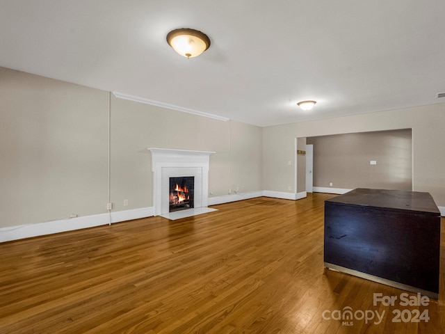 unfurnished living room with a fireplace with flush hearth, wood finished floors, visible vents, and baseboards