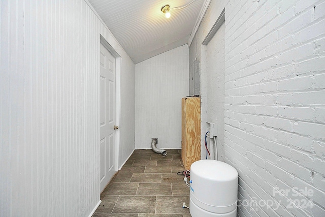 bathroom featuring lofted ceiling, toilet, and brick wall