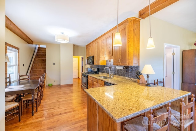 kitchen featuring kitchen peninsula, hanging light fixtures, stainless steel range with gas stovetop, light hardwood / wood-style floors, and sink