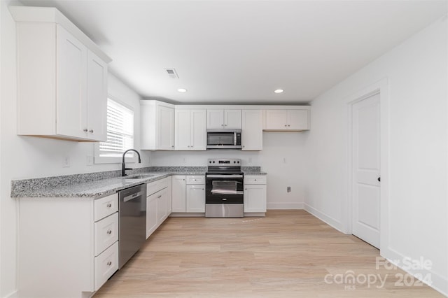 kitchen with stainless steel appliances, sink, light stone countertops, white cabinetry, and light hardwood / wood-style floors