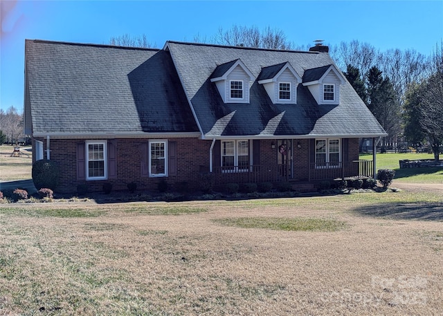 view of front of property with covered porch, brick siding, a shingled roof, a front lawn, and a chimney