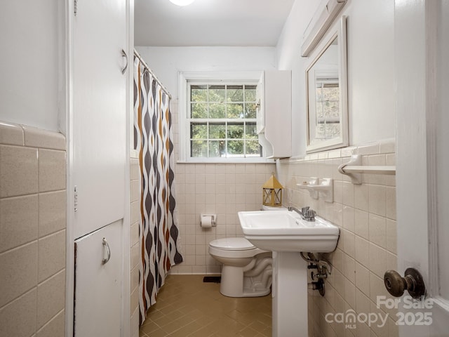 full bathroom with toilet, curtained shower, a wainscoted wall, and tile walls