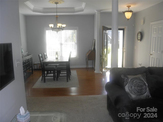 living room with wood-type flooring, an inviting chandelier, decorative columns, a raised ceiling, and crown molding