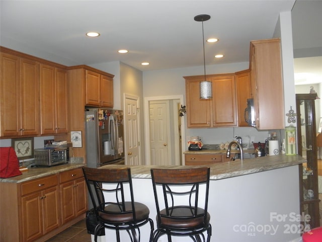 kitchen featuring light stone counters, stainless steel appliances, dark tile patterned floors, pendant lighting, and kitchen peninsula