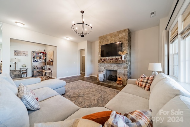 living room featuring a stone fireplace, dark hardwood / wood-style flooring, and an inviting chandelier