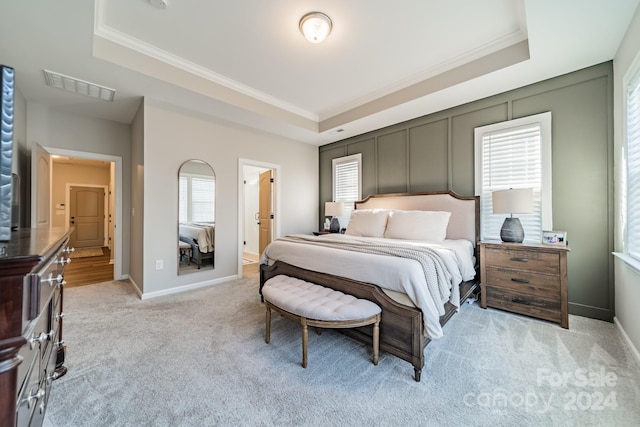 carpeted bedroom featuring a tray ceiling, ensuite bath, and ornamental molding