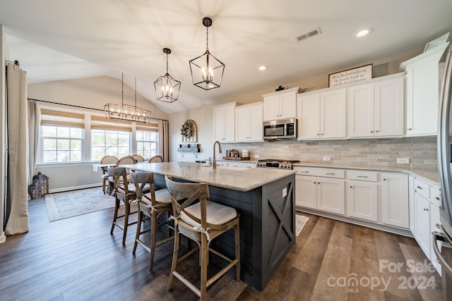 kitchen with stainless steel appliances, dark hardwood / wood-style floors, an island with sink, lofted ceiling, and white cabinets