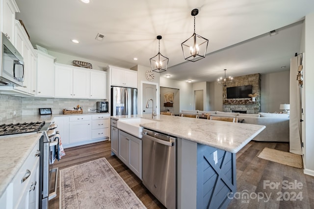 kitchen featuring white cabinets, a stone fireplace, sink, an island with sink, and stainless steel appliances