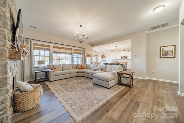 living room featuring hardwood / wood-style floors, an inviting chandelier, and a stone fireplace