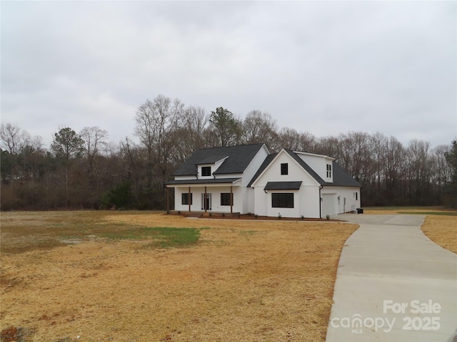 modern inspired farmhouse with a garage, covered porch, driveway, and a front lawn