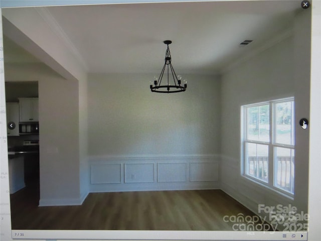 unfurnished dining area with a wainscoted wall, crown molding, a notable chandelier, visible vents, and wood finished floors