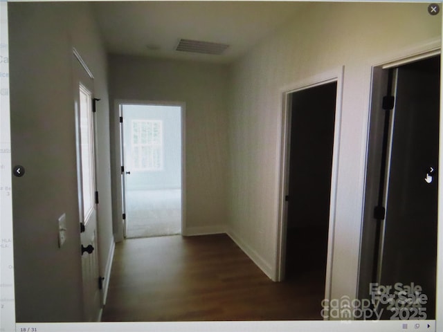 corridor with dark wood-style floors, visible vents, and baseboards