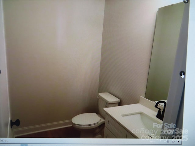 half bath with baseboards, vanity, and toilet