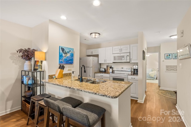 kitchen with white cabinetry, light stone counters, kitchen peninsula, hardwood / wood-style floors, and white appliances