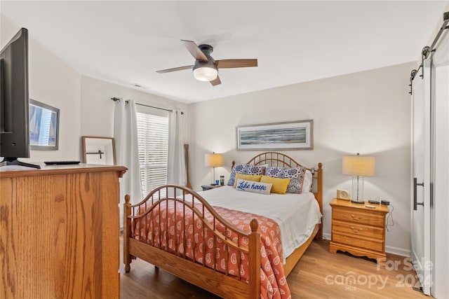 bedroom featuring a barn door, ceiling fan, and hardwood / wood-style floors