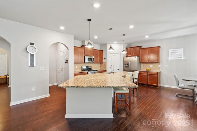 kitchen featuring a kitchen breakfast bar, arched walkways, appliances with stainless steel finishes, and dark wood-style flooring