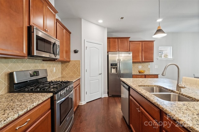 kitchen with a sink, stainless steel appliances, light stone counters, and dark wood-style flooring