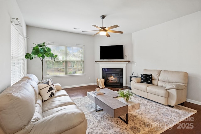 living area with a glass covered fireplace, visible vents, a ceiling fan, and wood finished floors