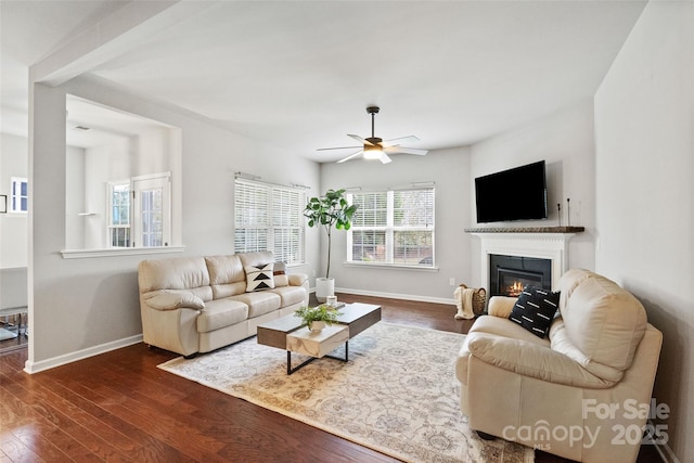 living room with a glass covered fireplace, baseboards, dark wood-style flooring, and ceiling fan