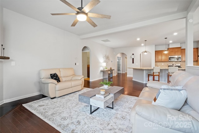 living area with dark wood-type flooring, beamed ceiling, visible vents, and arched walkways