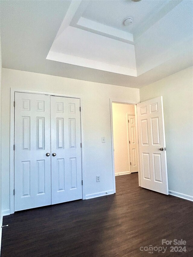 unfurnished bedroom featuring dark hardwood / wood-style floors, a raised ceiling, and a closet