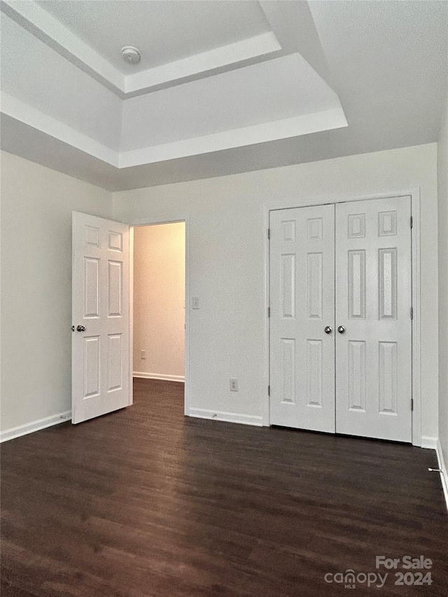 unfurnished bedroom featuring a raised ceiling, dark hardwood / wood-style flooring, and a closet