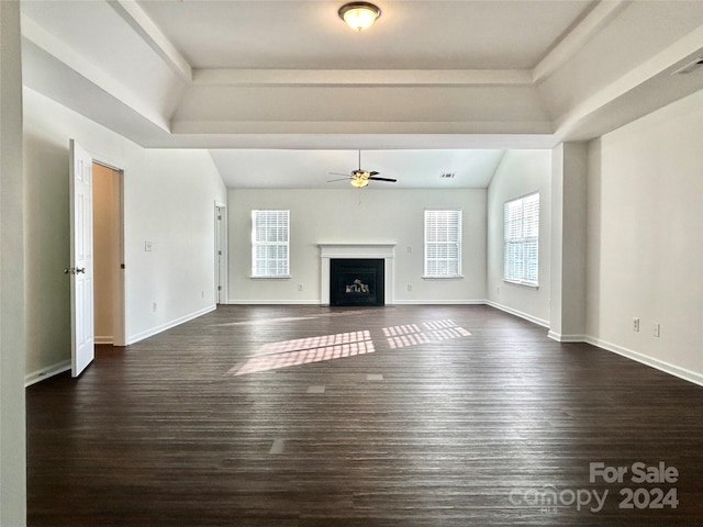 unfurnished living room with a tray ceiling, ceiling fan, and dark wood-type flooring