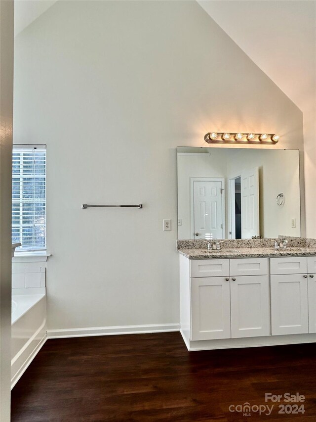 bathroom featuring a tub, hardwood / wood-style floors, vanity, and vaulted ceiling