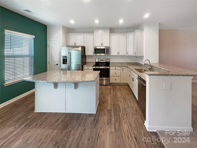 kitchen with appliances with stainless steel finishes, sink, kitchen peninsula, white cabinets, and dark hardwood / wood-style floors