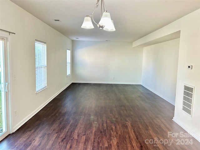 spare room with dark hardwood / wood-style floors and an inviting chandelier