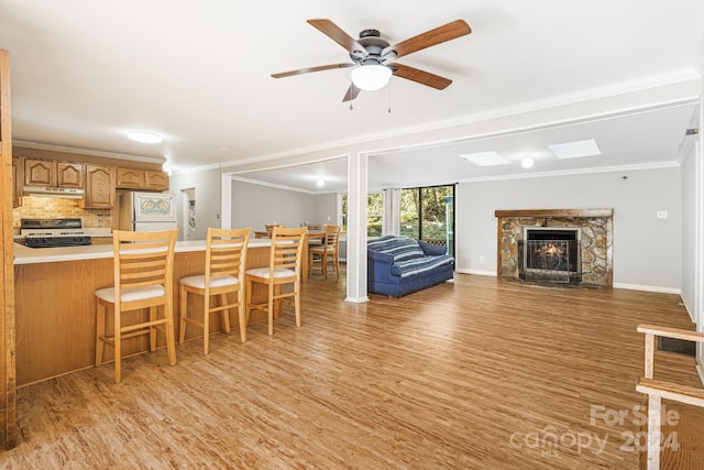 living room with a stone fireplace, ornamental molding, light wood-type flooring, and ceiling fan