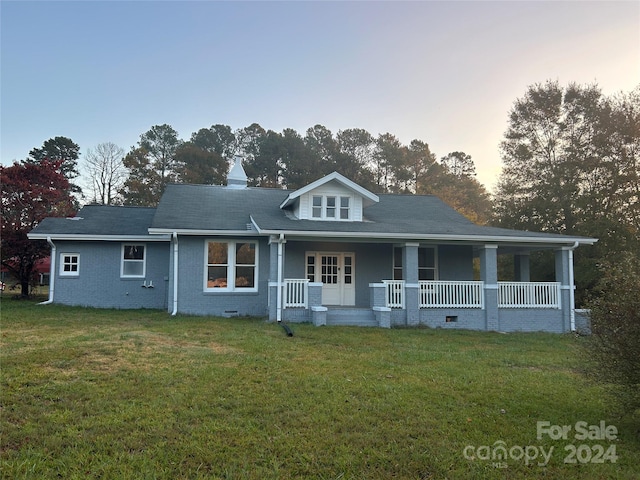 back house at dusk featuring a yard and a porch