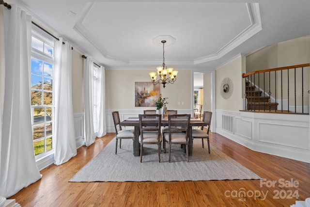 dining room with a healthy amount of sunlight, wood-type flooring, and a raised ceiling