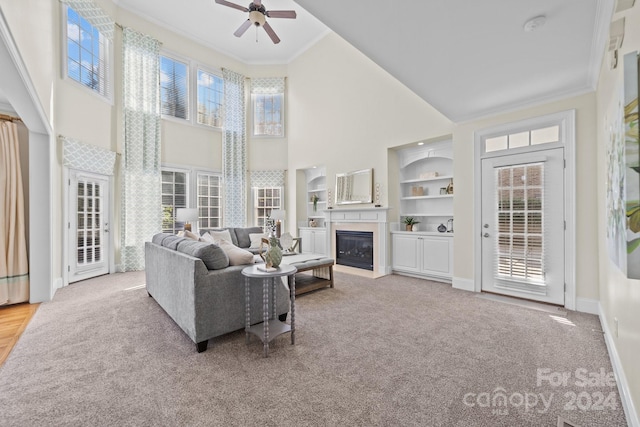 carpeted living room featuring a towering ceiling, ornamental molding, ceiling fan, and built in shelves