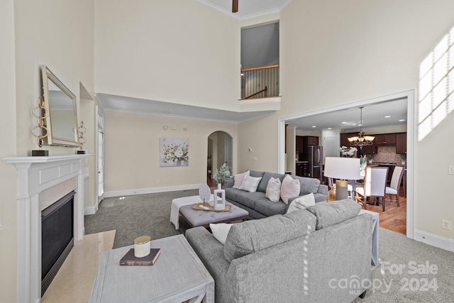 carpeted living room featuring a premium fireplace, a notable chandelier, ornamental molding, and a high ceiling