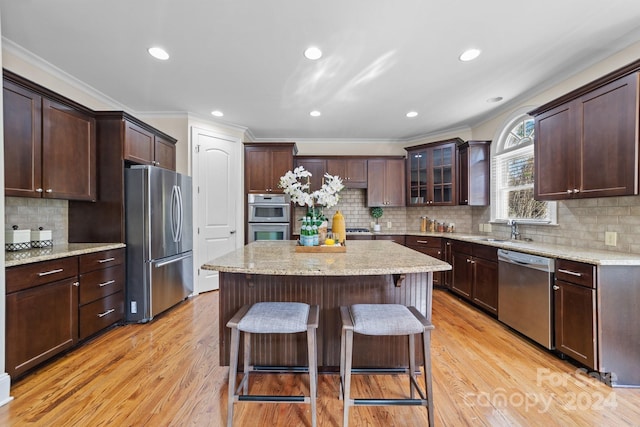 kitchen featuring a kitchen island, a breakfast bar area, stainless steel appliances, crown molding, and light hardwood / wood-style floors