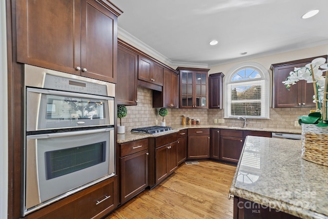 kitchen with sink, light stone counters, stainless steel appliances, and light wood-type flooring