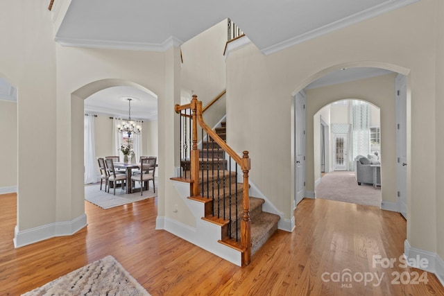 stairs featuring an inviting chandelier, hardwood / wood-style floors, and crown molding