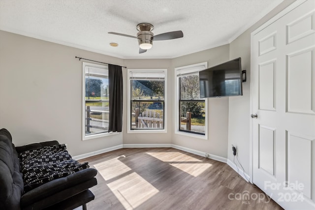 living area featuring crown molding, a textured ceiling, light wood-type flooring, and ceiling fan